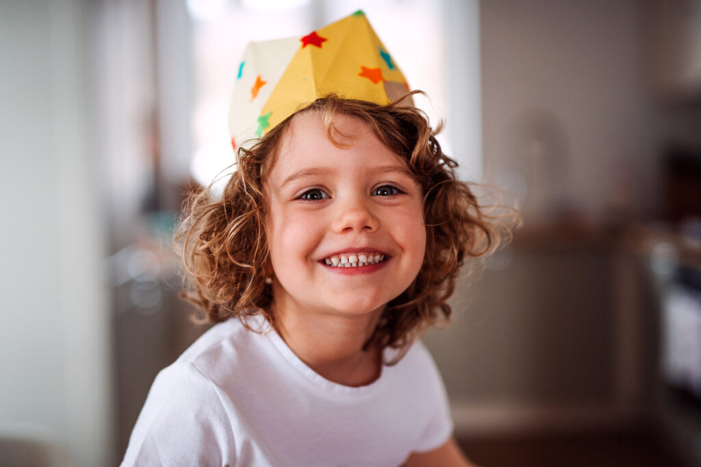 A portrait of small girl with a paper crown at home, looking at camera.