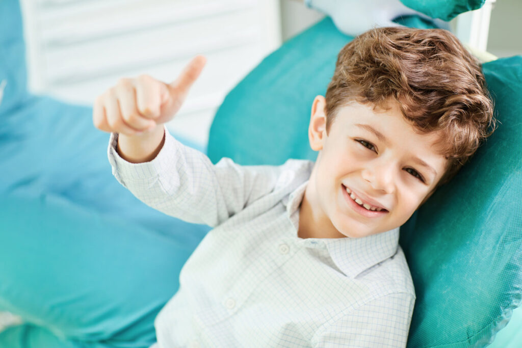 The boy smiles raised his thumb up in the dentist's chair.