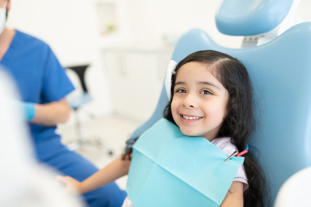 Smiling cute Hispanic girl sitting on chair at dental clinic