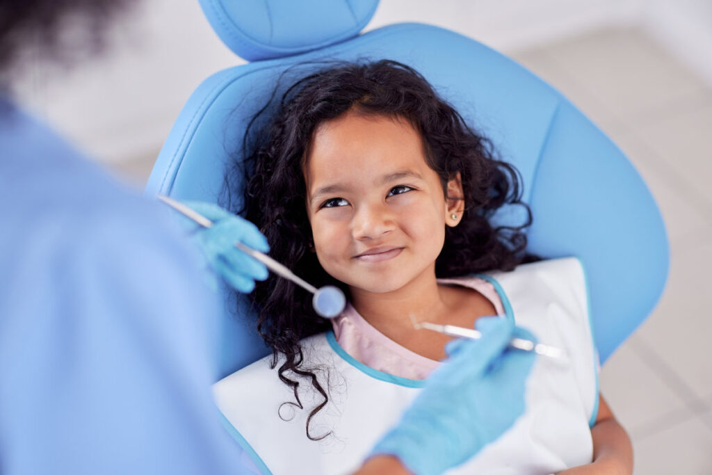 Dentistry, happy and kid patient at dentist for teeth cleaning, oral checkup or consultation. Healthcare, smile and girl child laying on chair for dental mouth examination with equipment in a clinic