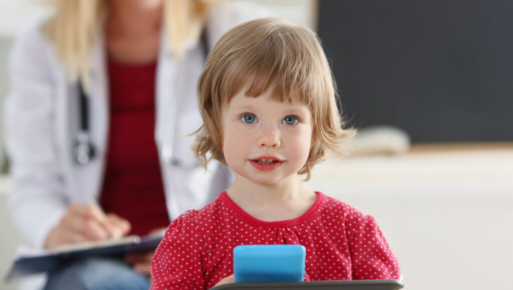 Portrait of little girl on background of doctor in white coat. Child examination and medical care concept