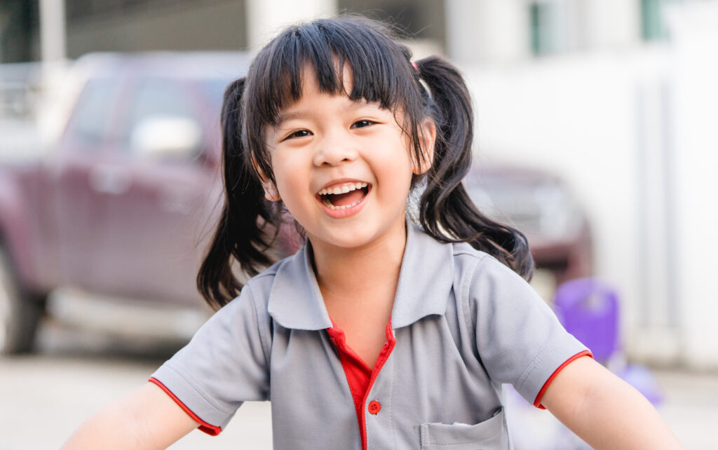 Happy Little asian girl child showing front teeth with big smile and laughing : Healthy happy funny smiling face young adorable lovely female kid.Joyful portrait of asian elementary school student.