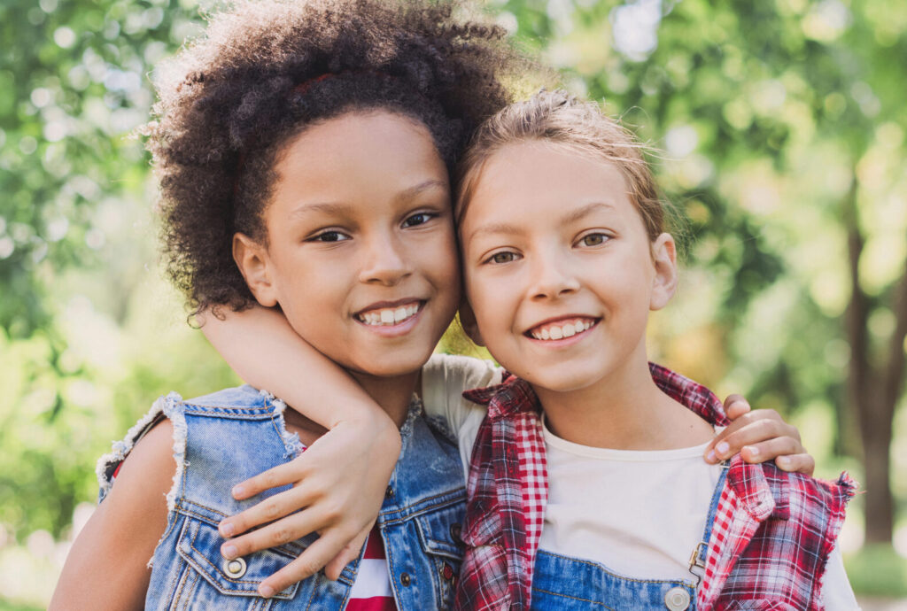 Two little girls hugging in the park. Diverse multi ethnic kids friends playing together outdoor. Summer fun, friendship, diversity, vacations concept