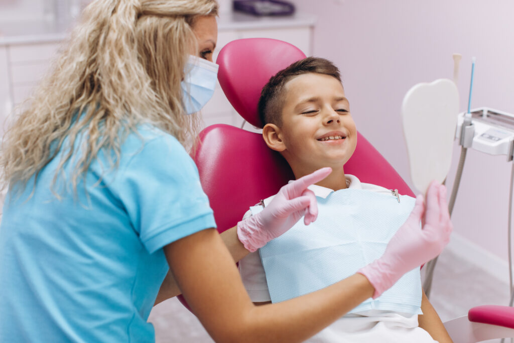 Woman dentist holds a mirror and shows a smiling boy his new beautiful smile after a visit to the dental clinic