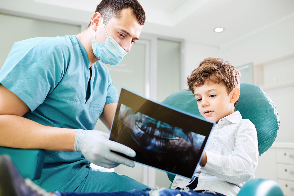 Boy child and dentist look at x-ray image in the dental office.