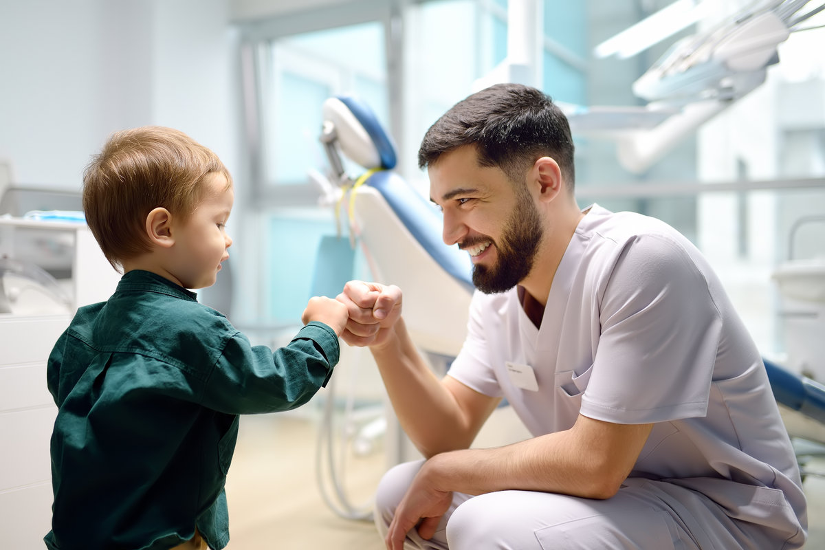 Friendly dentist greets cute toddler boy in office. Doctor encouraging with small child patient and giving him "high five". Kids doc establishes contact and trust with little patient