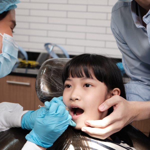 Asian female pediatric dentist examines a girl's teeth in dental clinic and takes care and encourages of father, mouth oral hygiene, and professional orthodontic healthcare work in a kid hospital.