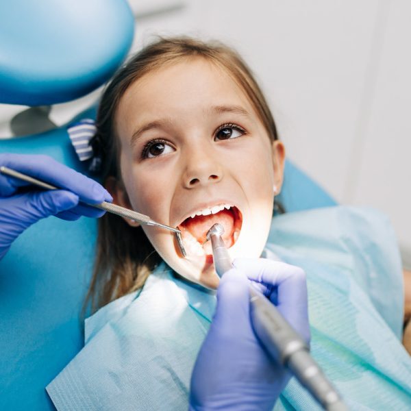 Cute little girl sitting on dental chair and having dental treatment.