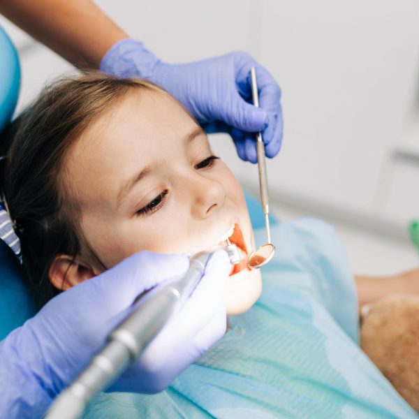 Cute little girl sitting on dental chair and having dental treatment.