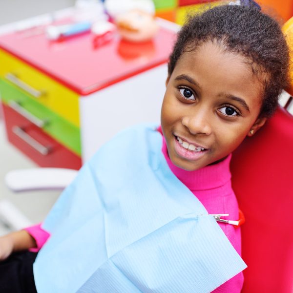 cute black baby girl smiling sitting in a red dental chair at the examination at the children's dentist