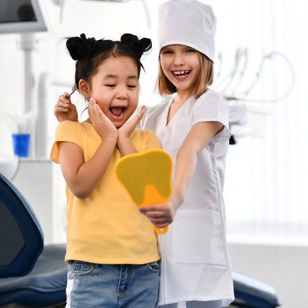 Kids girls play dentist and happy patient in dental office. Patient and stomatologist are glad to see patient healthy smile.