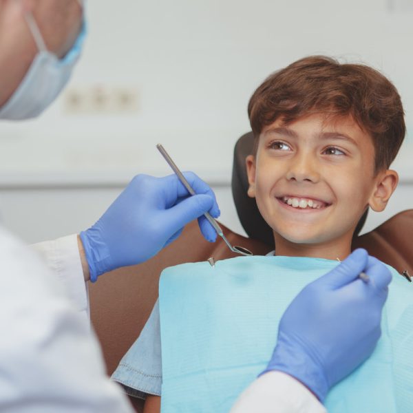Adorable happy healthy boy smiling cheerfully at his dentist, sitting in a dental chair. Cropped shot of a professional dentist checking teeth of a lovely boy