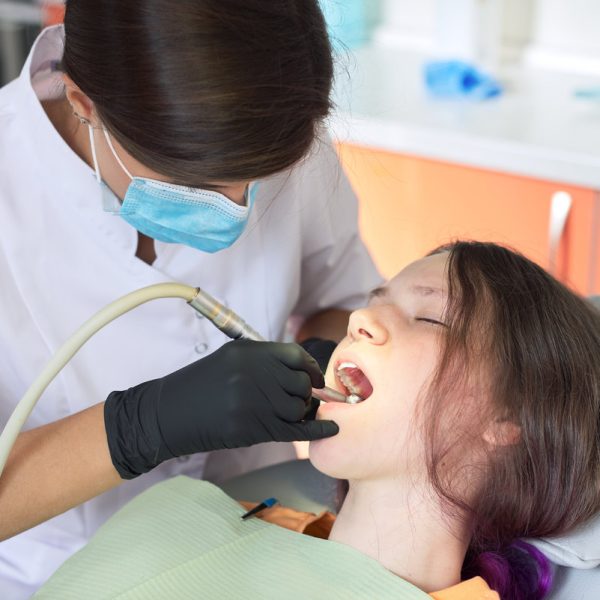 Woman dentist treating teeth to a patient sitting in dental chair using professional equipment. Dentistry, healthy teeth, sedation, medicine and healthcare concept