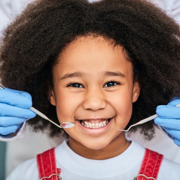 African American little girl with a toothy smile during an inspection of oral cavity by a dentist. Child in a dental clinic for children, cropped