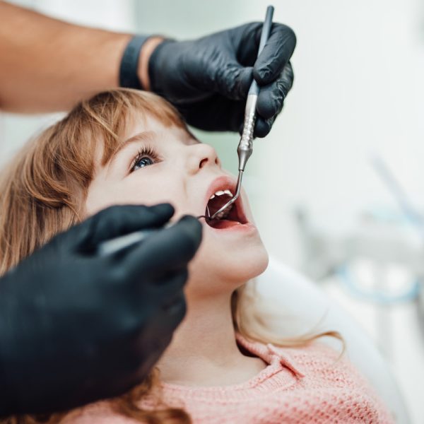 Cute little girl sitting on dental chair and having dental treatment.