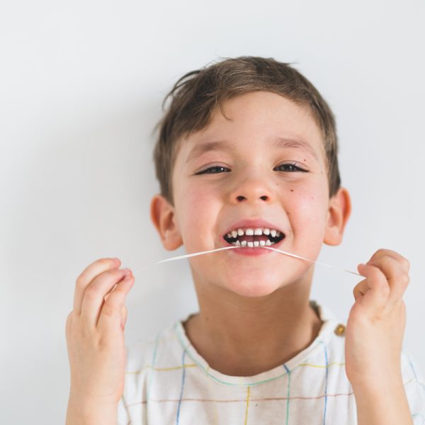 Cute boy pulling loose tooth using a dental floss. The boy's first milk tooth is loose. Toothache. Process of removing a baby tooth. Emotions of a child