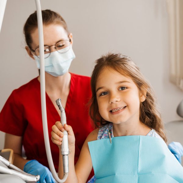 Cheerful girl child holding dental drill and smiling in dentistry. The child smiles at the consultation with the dentist