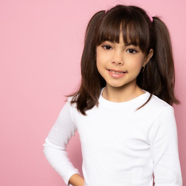 Close up head shot portrait image with smiling little brown-haired girl. Concept happy and beauty kid with good healthy teeth for dental on pink background, eight year child looking at camera and posing