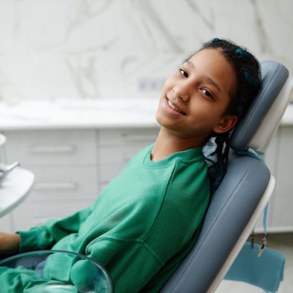 Portrait of black teenage girl sitting in dental chair and smiling at camera during checkup