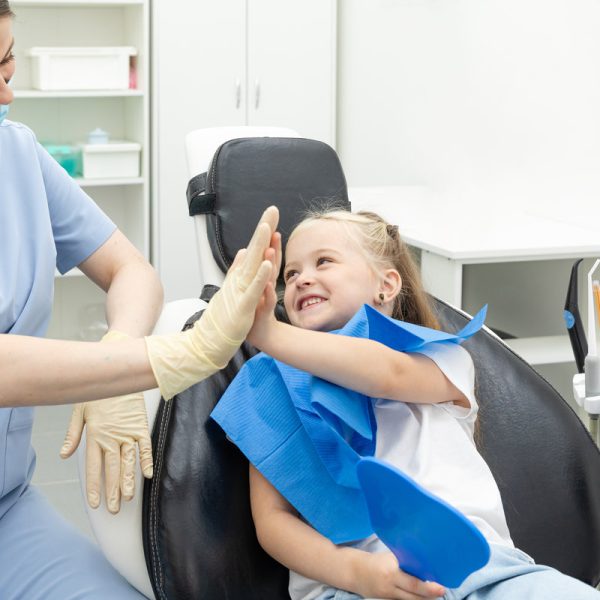 Little patient girl sitting in a chair gives a high five to a pediatric dentist after dental treatment at a clinic with modern equipment. Concept of modern and painless treatment of children's teeth.