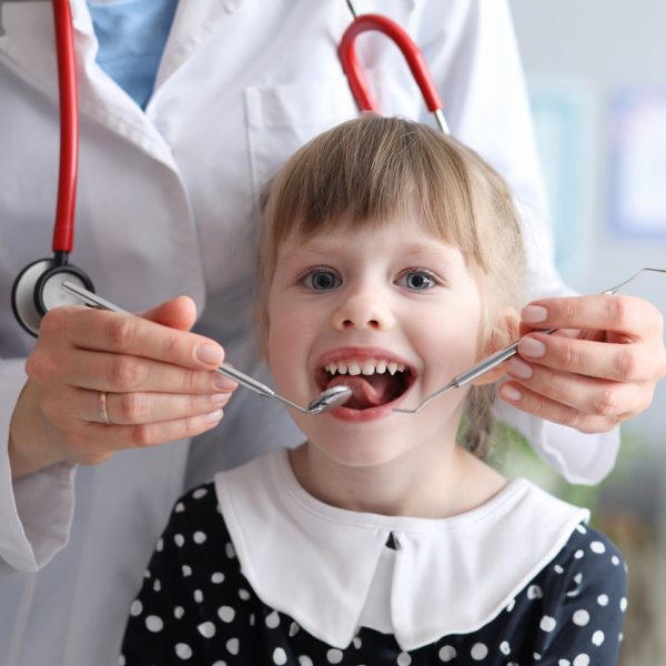 Little girl is not afraid to show teeth to dentist. Prophylactic examinations child at dentist. High-quality dental treatment. Doctor will examine oral cavity and evaluate result previous treatment