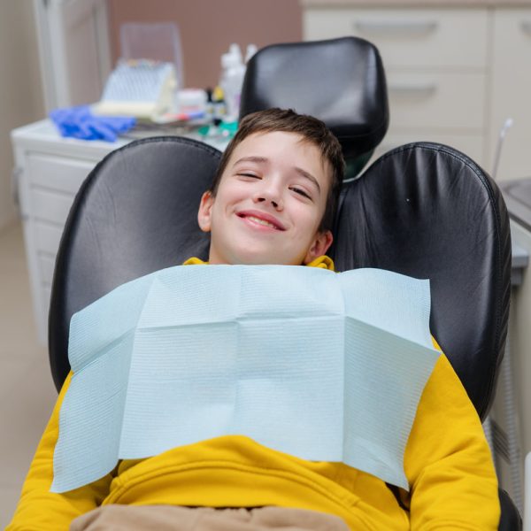 Cute little boy is sitting in a dental chair with a happy expression on his face, glad to treat his teeth. Prevention of diseases of baby teeth in children.